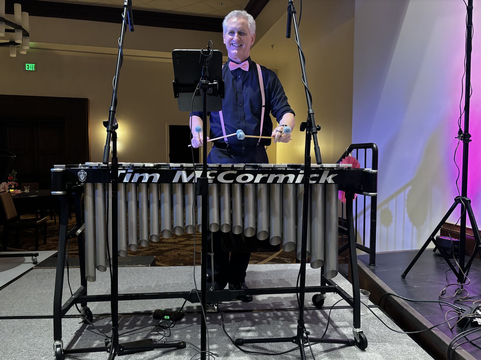Tim McCormick smiling behind his vibraphone, wearing a black shirt with a pink bow tie and pink suspenders, mallets in hand, at the Pink Fling
